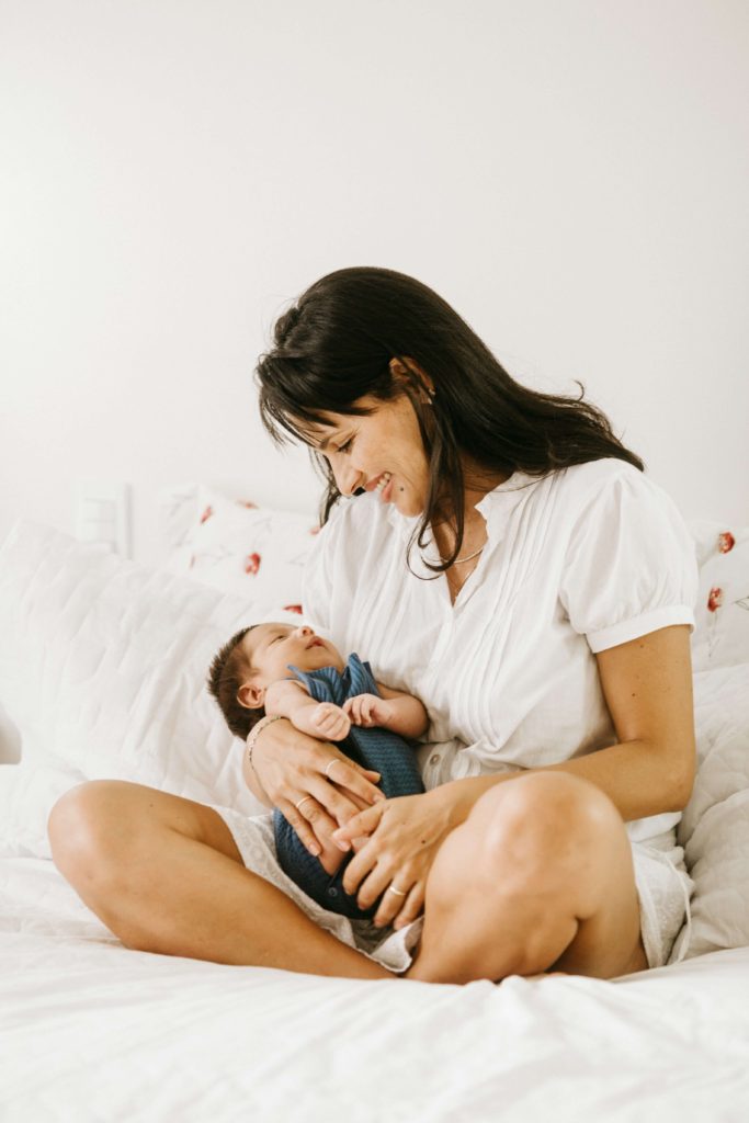 A small baby in the arms of his smiling mother on a white bed